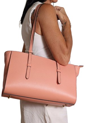 Vrouw in wit mouwloos topje met een grote, textuurige roze leren schoudertas met dubbele bandjes en gouden metalen voetjes.