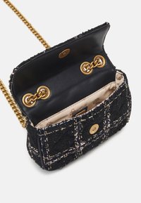 Tweed crossbody taske i sort med guldlukning, med en quiltet mønster og satininteriør. Kædesti og trykknapslukning.