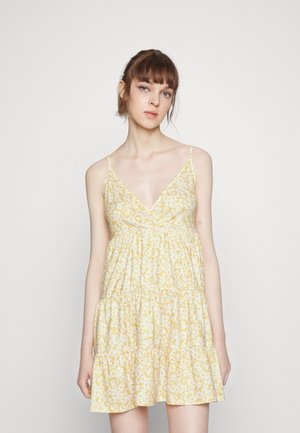 Vestido amarelo floral com decote em V, alças finas e saia em camadas. Apresenta um tecido leve com uma textura suave e pequenos padrões de flores brancas.