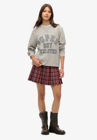 Szary sweatshirt z nadrukiem "SUPER DRY ATHLETICS", w połączeniu z czerwoną spódnicą w kratę z plisami oraz czarnymi skórzanymi botkami do kolan.