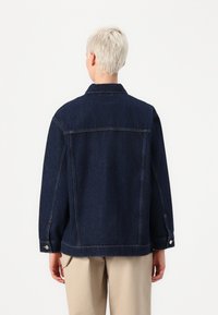 Jeans jakna temno modre barve, z ovratnikom, dolgimi rokavi in gumbi na manšetah. Gladka tekstura z vidnimi šivi.