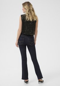 Top senza maniche nero con paillettes abbinato a jeans flare in denim scuro. I jeans presentano tasche posteriori e un design aderente, accentuando la silhouette.