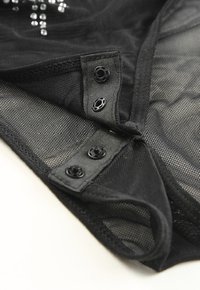 Black mesh garment featuring button closures, a soft texture, and subtle shine. The fabric has a sheer quality with a structured design.