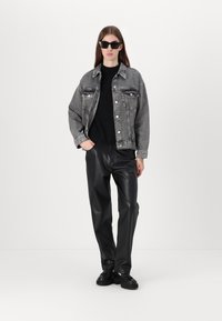 Denim jacket in gray with two chest pockets, paired with a black textured sweater and black faux leather pants, completed with black shoes.