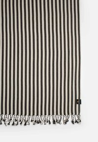Coperta a righe con colori alternati nero e crema, con bordi frangiati e un'etichetta in un angolo. Finitura in tessuto morbido e tessuto.
