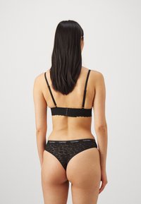 Sort med svart blonde som har en delikat bølget kant, med justerbare stropper og en matchende tang med en merket midje.