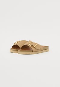 Sandales glissantes en suède beige avec une large sangle et une boucle en métal doré en forme de cercle. Semelle intérieure rembourrée et semelle en caoutchouc pour le confort.
