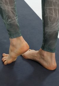 Groen gemusterde leggings met een gestructureerde afwerking, strak bij de enkel, gecombineerd met blote voeten die op een blauwe mat rusten.