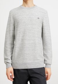 Sweatshirt gris clair avec un motif rayé texturé, col et poignets côtelés, comportant un petit logo brodé sur la poitrine.