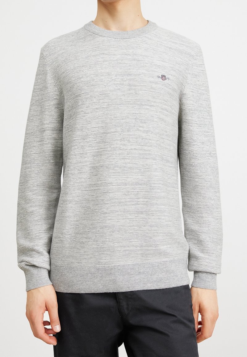 Sweatshirt gris clair avec un motif rayé texturé, col et poignets côtelés, comportant un petit logo brodé sur la poitrine.