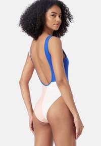 Bañador de una pieza que presenta una sección superior azul y una sección inferior con bloques de color en blanco y rosa claro, con un diseño de corte alto en la espalda.