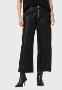 Pantaloni larghi neri realizzati in un materiale lucido, con vita alta, tasche frontali e cinque bottoni argentati lungo il davanti.