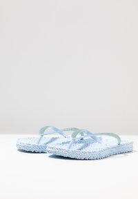 Světle modré žabky s texturovanou tkanou podrážkou, s lesklými průhlednými popruhy a třpytivými detaily podél okrajů popruhů.