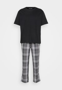 Must black short-sleeve t-särk, mille juurde kuuluvad hallid ruudulised püksid, mis on kaunistatud valgete ja roheliste triipudega; püksid on alt laiemad.