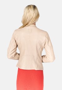 Helle beigen Lederjacke mit tailliertem Design, ausgestattet mit Nahtdetails und einem quadratischen Logo-Patch im oberen Rückenbereich.