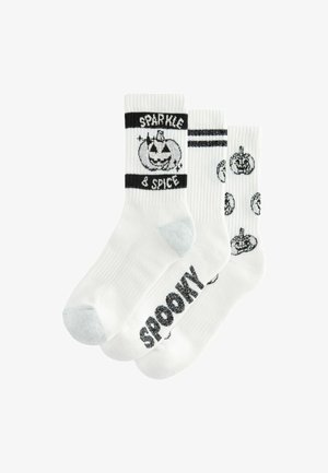 Tri par bijelih čarapa s crnim dizajnom: jedan s natpisom "SPOOKY," drugi s grafikom bundeve, i pojasom sa prugama. Mekana tekstura.