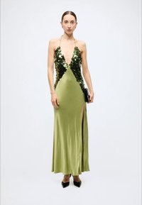 Sleeveless green gown features a plunging neckline, sequin detailing, a thigh-high slit, and a smooth satin finish. Black clutch and heels included.