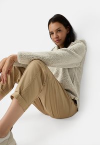 Crème textuur fleece hoodie met een kwartrits, gecombineerd met lichtbeige opgerolde broeken en neutraalgekleurde schoenen.