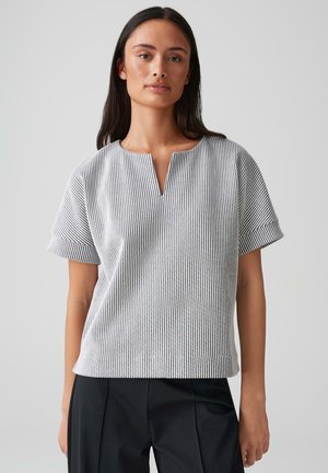 Striped short-sleeve blouse with a round neckline and a front placket. Fabric has a textured, woven appearance in black and white.