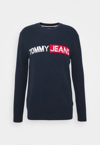 Granatowy sweter z długim rękawem o prążkowanej fakturze, z logo "TOMMY JEANS" w białym i czerwonym kolorze na piersi.