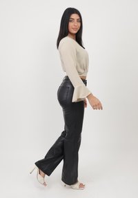 Haut beige court avec des manches évasées, associé à un pantalon noir en cuir synthétique taille haute et des sandales blanches à talons ouverts avec un motif en grille.