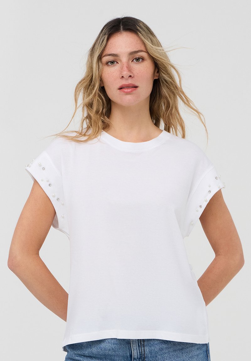 T-shirt bianco a maniche corte in cotone, con accenti di perle decorative sui risvolti delle maniche e un design oversize.