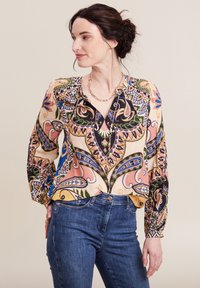 Langärmlige Bluse aus gemustertem Stoff mit einer Mischung aus Blumen- und Paisleymustern in lebhaften Farben, kombiniert mit dunklen Jeans.