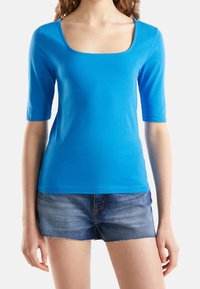 Modrý top s krátkými rukávy a čtvercovým výstřihem, vyrobený z měkké látky, v kombinaci s džínovými šortkami s třepenými okraji.