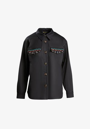 Chemise noire à boutons, à manches longues, avec deux poches poitrine et des perles décoratives le long des bords des poches. Texture de tissu lisse.