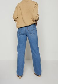 Jean en denim bleu clair à coupe décontractée, doté d'un design à cinq poches et d'une petite étiquette de marque rouge sur la ceinture arrière.