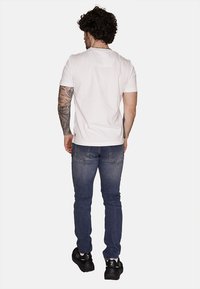 Maglietta bianca in cotone con maniche corte, abbinata a jeans blu scuro. L'outfit presenta un design semplice e una silhouette aderente.