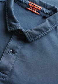 Polo azul marino hecho de algodón texturizado, con tapeta de botones y cuello estructurado. Etiqueta de la marca visible en el escote.