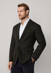 Mörkgrön rutigt kavaj tillverkad av texturerat tyg, med två framfickor, träknappar och en notch-lapel design.
