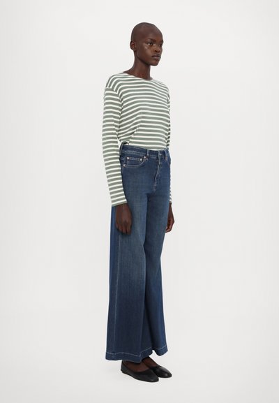 Stripet langermet skjorte i grønn og hvit, kombinert med vide mørkeblå jeans. Svart flate sko fullfører antrekket.