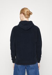 Felpa con cappuccio di colore blu navy, con cappuccio, maniche lunghe e una texture morbida. Presenta una vestibilità comoda e un'etichetta con logo discreta vicino all'orlo.