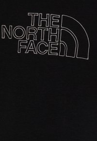 Tessuto di cotone nero con тексто ricamato bianco che recita "THE NORTH FACE" e un logo a mezza luna.
