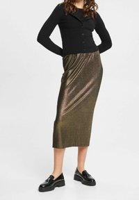 Zwarte geribbelde cardigan met knopen, gecombineerd met een metallic bronzen, knielange rok met een gladde textuur en diagonale ribbels; gedragen met zwarte oxford schoenen.