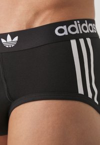 Sorte Adidas boxershorts med en hvid mærkevare-vingebånd, der har tre vertikale hvide striber på siden og en tætsiddende pasform.
