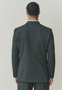 Blazer sombre à texture, avec une coupe cintrée, doté d'une fente centrale, de revers crantés et de deux boutons. La vue arrière révèle un motif subtil.