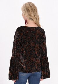 Černý sametový top s paisley vzorem v oranžové a zlaté barvě. Obsahuje zvonové rukávy a kulatý výstřih, v kombinaci s modrými džíny.