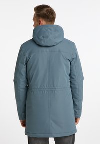 Parka impermeabile blu con cappuccio, maniche lunghe e vita cinchata. Texture liscia, design minimalista e taglio lungo fino al ginocchio.