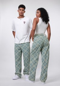 Casual outfit featuring a white oversized T-shirt and green plaid trousers with a relaxed fit, complemented by white sneakers.