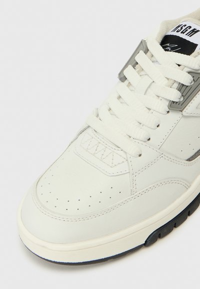 Weiße Ledersneaker mit perforierten Details auf der Zehenkappe, runden Schnürsenkeln und grauen Akzenten. Gummisohle mit einem dunkelblauen Boden.
