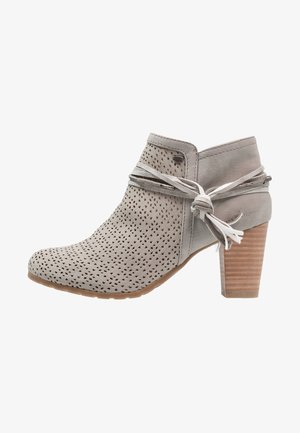 Bottine en daim gris clair avec motifs découpés au laser, lacets en cuir noués en nœud papillon, et talon bloc en bois empilé.