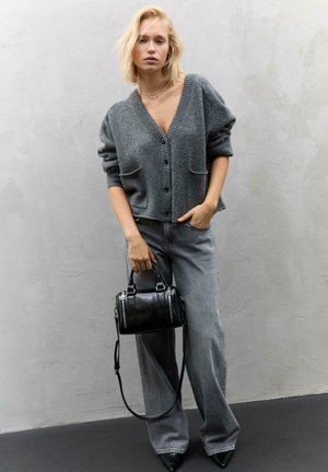 Grauer gestrickter Cardigan mit tiefem V-Ausschnitt und Fronttaschen, kombiniert mit lockeren grauen Jeans und einer kleinen schwarzen Tasche mit glänzenden Hardware-Akzenten.