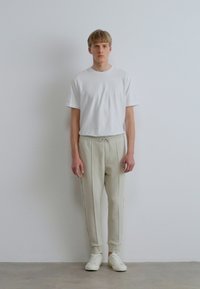 Valkoinen lyhythihainen t-paita yhdistettynä vaalean beigen sävyisiin kapeneviin verkkarihousuihin ja valkoisiin lenkkareihin. Yksinkertainen, minimalistinen design, jossa kiristysnauha vyötäröllä.