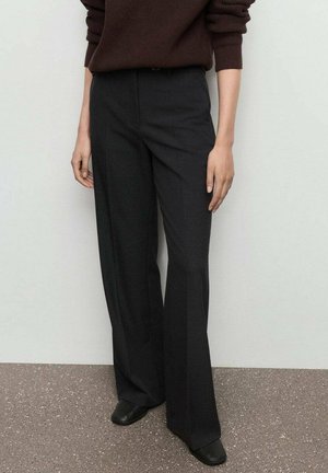 Pantalons larges noirs avec une texture lisse et une coupe ajustée, dotés d'une taille mi-haute et de plis avant. Portés avec des chaussures noires.