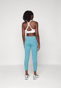 Biały biustonosz sportowy z krzyżowanym tyłem, w połączeniu z legginsami o średnim stanie w jasnoniebieskim kolorze. Legginsy mają teksturowane wykończenie oraz akcentujące szwy.