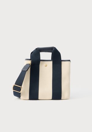 Petit sac fourre-tout beige en toile avec deux larges sangles verticales noires, une poignée courte et une bandoulière réglable avec boucle dorée.