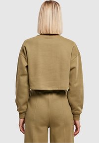 Felpa corta verde oliva con maniche lunghe, polsini a coste e una texture liscia. Presenta una vestibilità morbida e un design pulito e semplice.